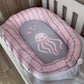 Baby nest with pink and gray striped border and jellyfish design in a crib.