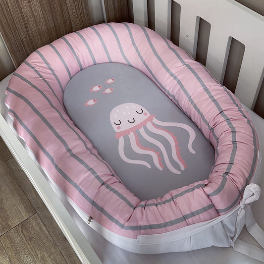 Baby nest with pink and gray striped border and jellyfish design in a crib.
