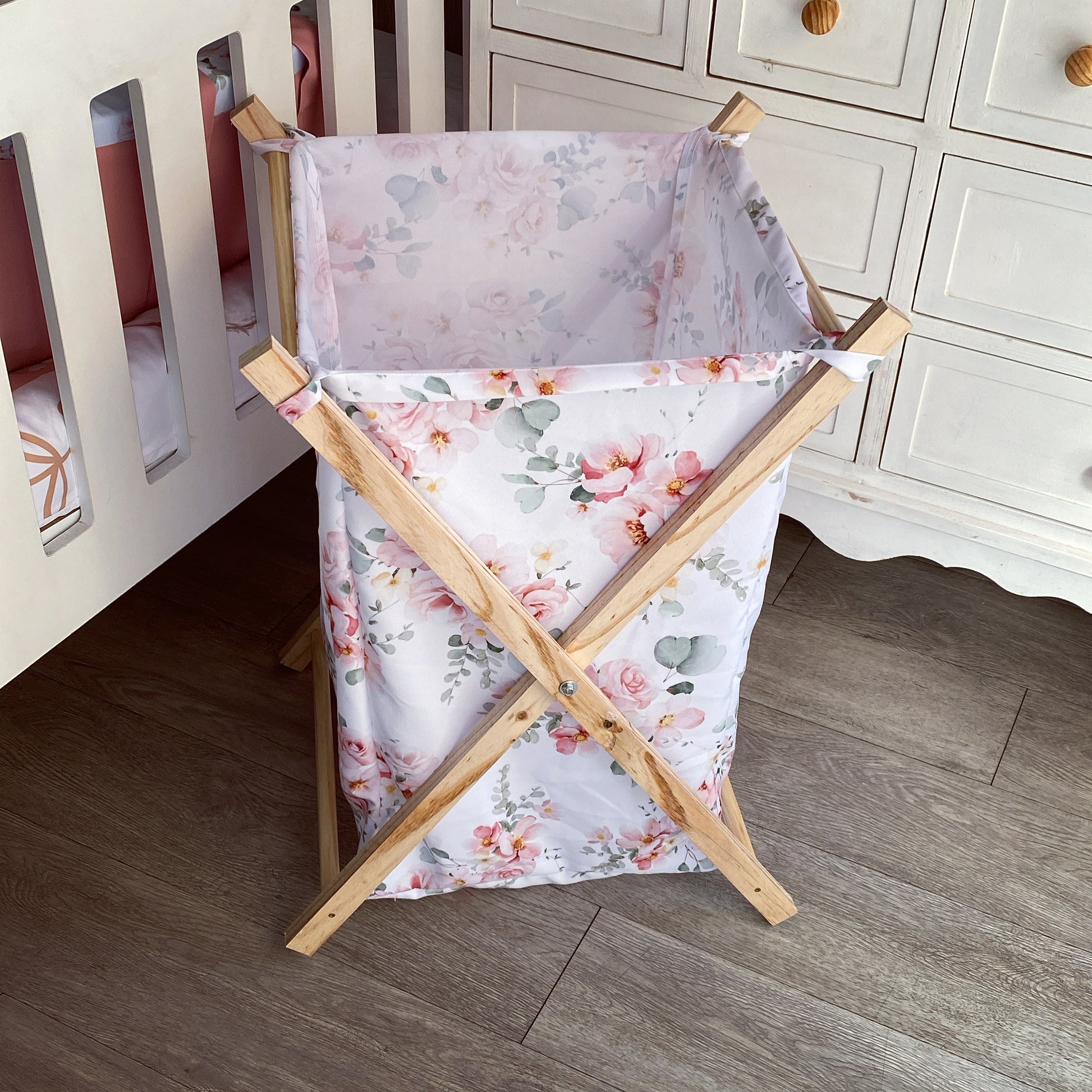 A wooden laundry basket with a pink floral pattern, featuring side handles and a five-point star base.