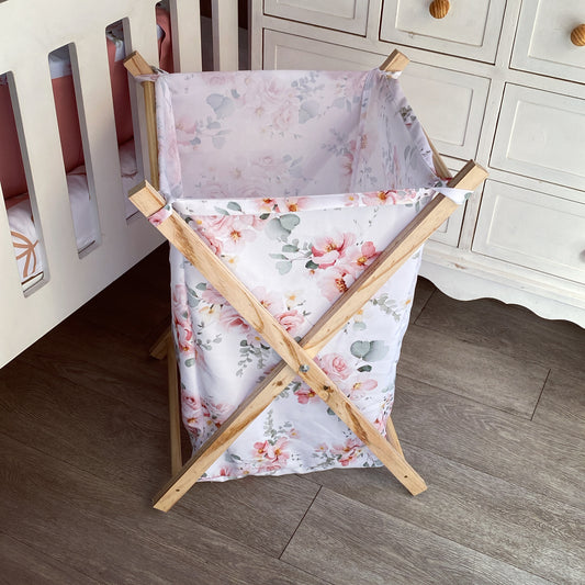 A wooden laundry basket with a pink floral pattern, featuring side handles and a five-point star base.