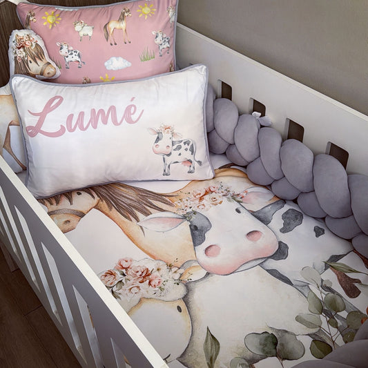 Crib with cow-themed bedding and decorative pillows in a nursery setting.
