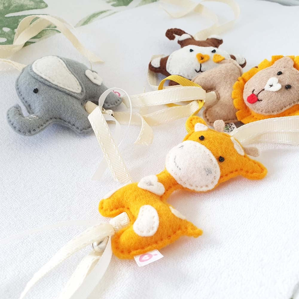 A set of handmade felt baby animal ornaments, including a gray elephant, orange giraffe, yellow lion, and brown/white zebra, decorated with cream ribbons.