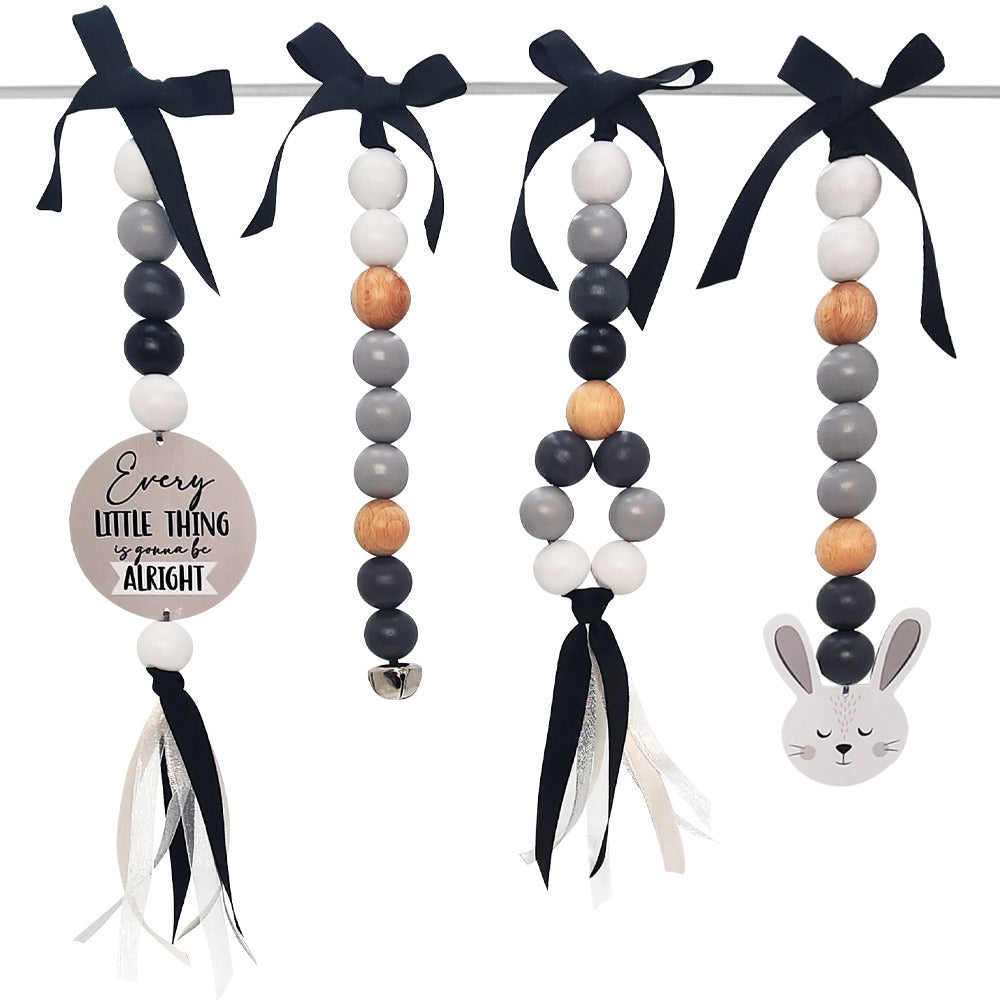 Easter bunny bead garland hanging from a white rod with black ribbon bows. The garland features wooden and painted beads in black, gray, white, and natural wood tones, a round wooden sign that reads 'Every LITTLE THING is gone be ALRIGHT', a small silver bell, and a white bunny head decoration at the end.