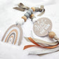 A baby teething toy or pacifier clip made with wooden beads, taupe ribbon, a round tag reading 'Here comes THE SUN,' and a rainbow-shaped tag on a soft white fabric background. | Baby Essentials | All Baby Products | Soft Spot Kids | South Africa
