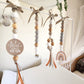 Three wooden bead baby mobiles hang from a white canopy in a nursery. The mobiles feature natural wood, white, and gray beads, tied with taupe ribbons at the top, and decorated with a round wooden sign reading 'Here comes THE SUN' and a small rainbow charm. | Baby Essentials | All Baby Products | Soft Spot Kids | South Africa