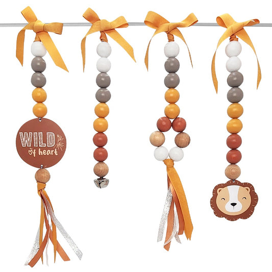 Three beaded baby hanging toys on a white background, each with orange and yellow ribbons, wooden beads in orange, brown, white, and gray, and decorative elements including a round 'WILD of heart' sign and a lion face.
