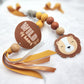 A decorative baby keepsake or gift tag featuring a lion face charm, wooden beads, yellow and brown ribbons, and a round brown tag that reads 'Wild of heart' on a soft white textured background. | Baby Essentials | All Baby Products | Soft Spot Kids | South Africa