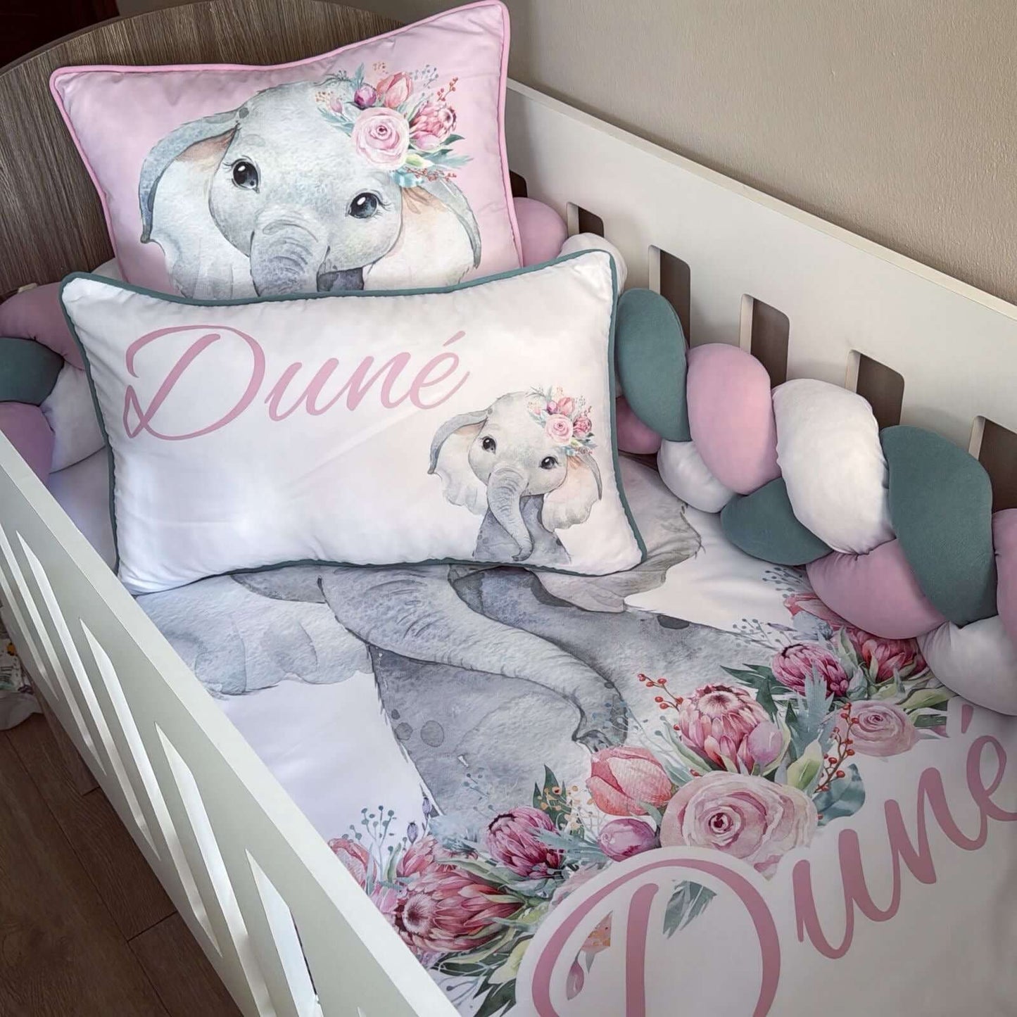 Children's crib with elephant-themed bedding and pillows featuring the brand 'Dune'.