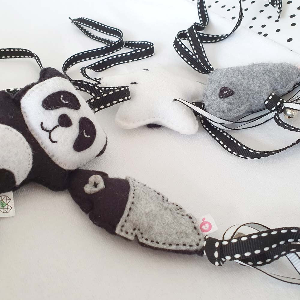 Three handmade felt baby toys with black and white polka-dot ribbon ties, including a panda, a star, and a whale, arranged on a white fabric background.