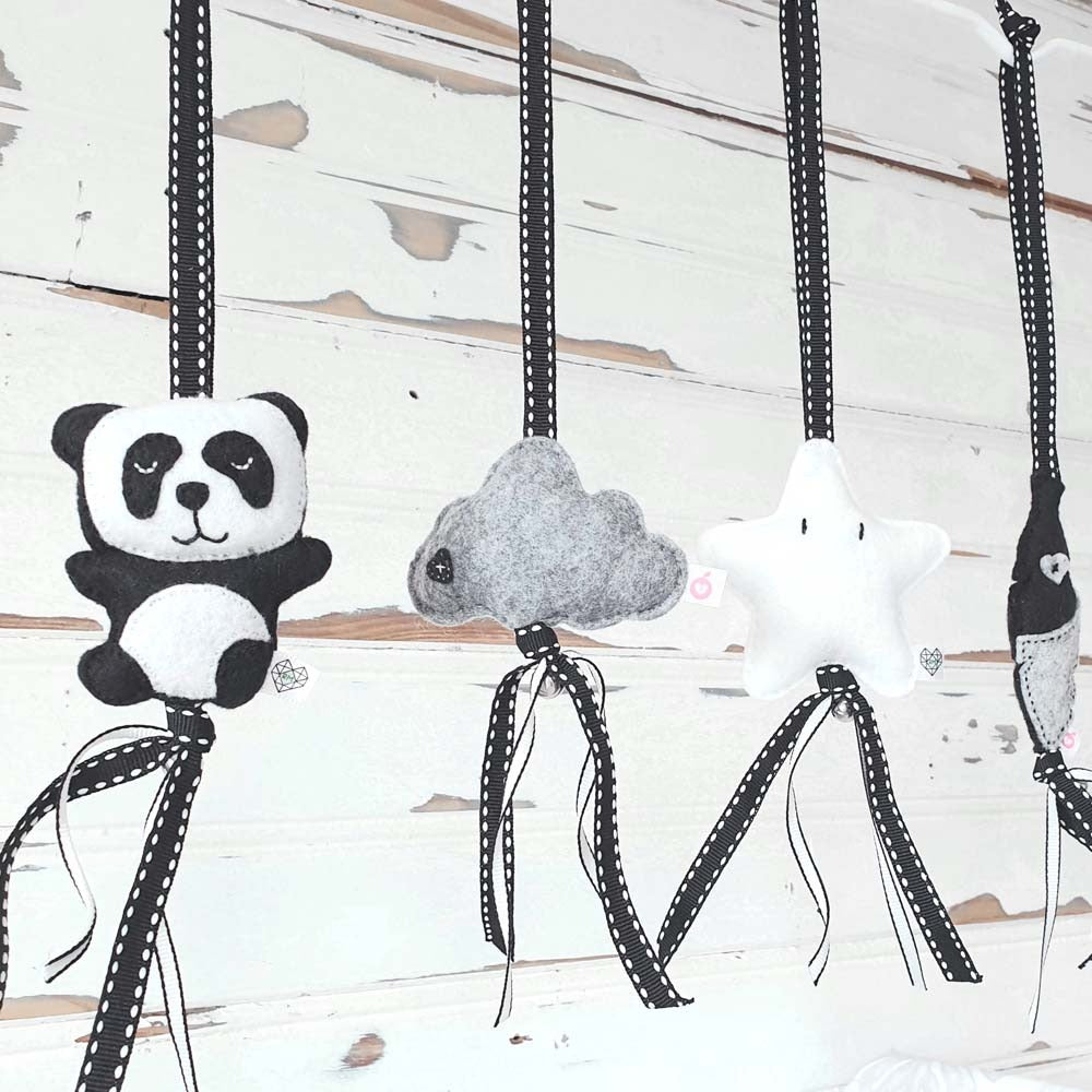 Felt baby nursery hanging decorations including a black and white panda, a gray cloud, a white star, and a fish, suspended from black and white polka-dotted ribbons against a distressed white wood background.