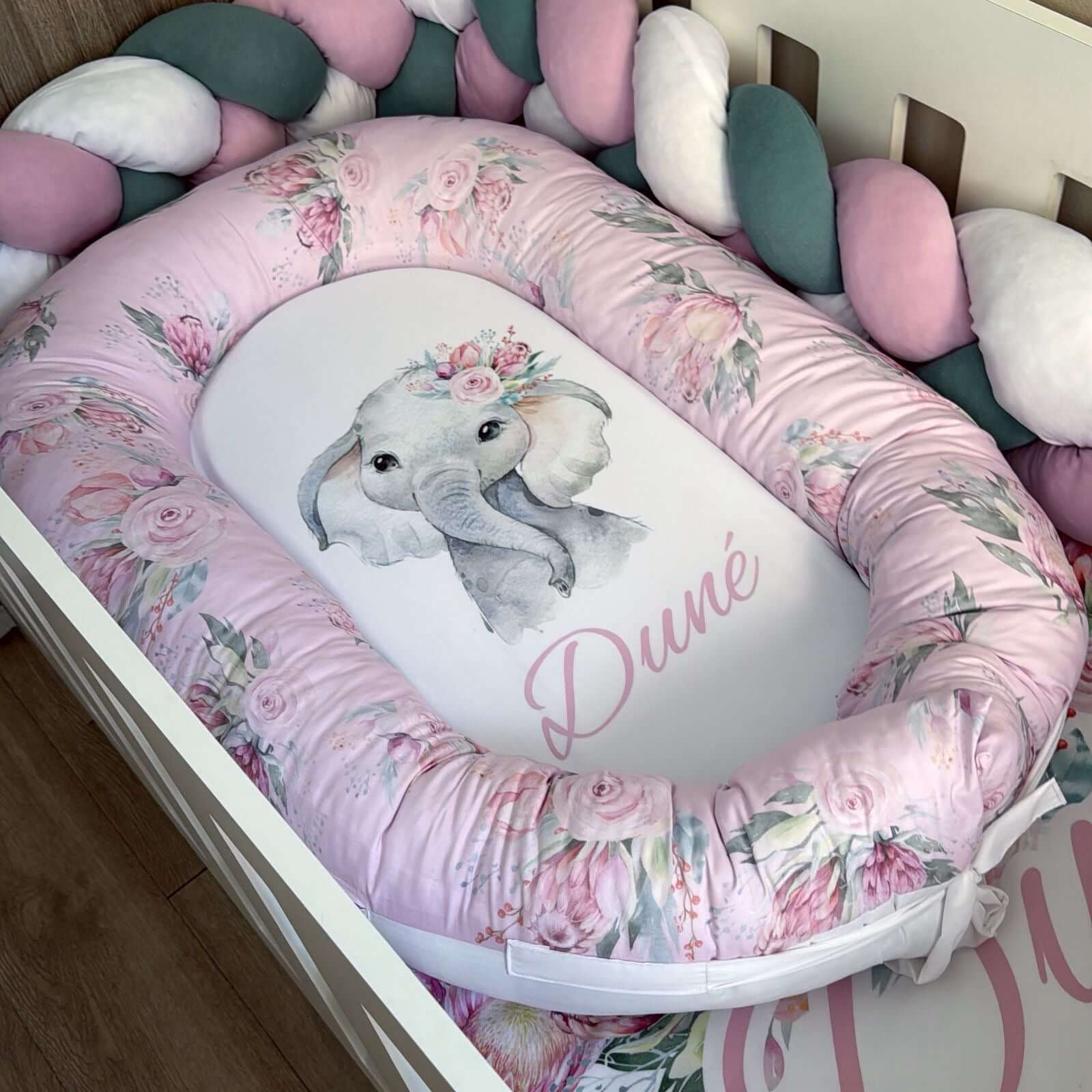 Baby crib bumper with floral design and elephant illustration, featuring the brand 'Dune'.