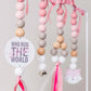 A close-up of a hanging beaded decoration with pastel pink, white, and light wood beads, pink ribbons, a round white tag reading 'WHO RUN THE WORLD,' and a small pink fox face charm. | Baby Essentials | All Baby Products | Soft Spot Kids | South Africa