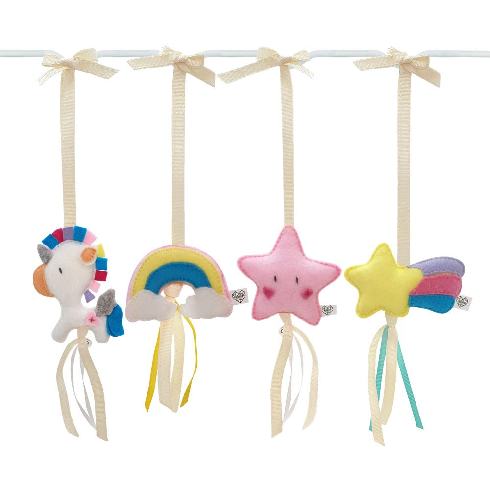 A set of four pastel-colored plush baby hanging toys on a white rod with cream ribbon ties. The toys include a white unicorn with a rainbow mane, a yellow and blue rainbow with white clouds, a pink star with a smiling face, and a yellow shooting star with blue and pink wings and cream ribbon tails.